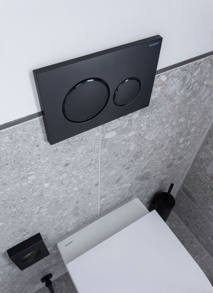 Czarny przycisk spłukujący Geberit Sigma20 zamontowany na ścianie nad wiszącą miską WC z zabudowanym stelażem podtynkowym Czarny przycisk spłukujący Geberit Sigma20 zamontowany na ścianie nad wiszącą miską WC z zabudowanym stelażem podtynkowym