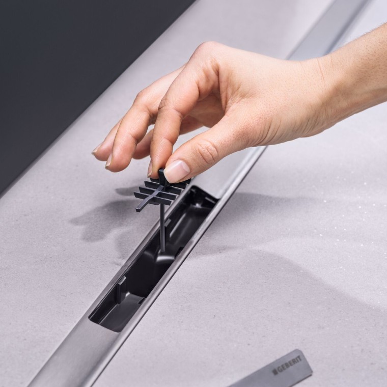 Dłoń umieszcza wkład grzebieniowy w odpływie liniowym Geberit Dłoń umieszcza wkład grzebieniowy w odpływie liniowym Geberit