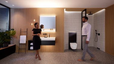 Mężczyzna i kobieta w doskonale oświetlonej łazience z meblami łazienkowymi i urządzeniami ceramicznymi Geberit ONE (© Geberit)