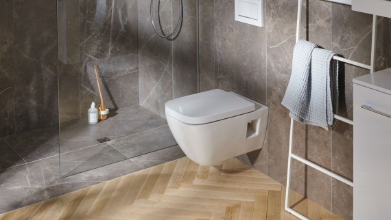 Na pierwszym planie miska WC. W tle kabina typu walk-in z wpustem podłogowym do natrysku Geberit