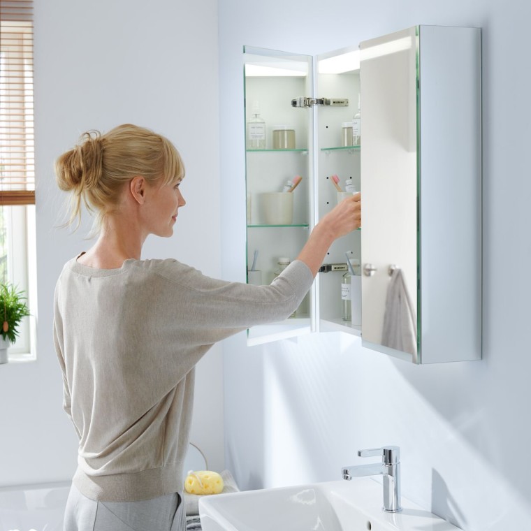 Młoda kobieta sięga do łazienkowej szafki z lustrem Gerberit Option Młoda kobieta sięga do łazienkowej szafki z lustrem Gerberit Option
