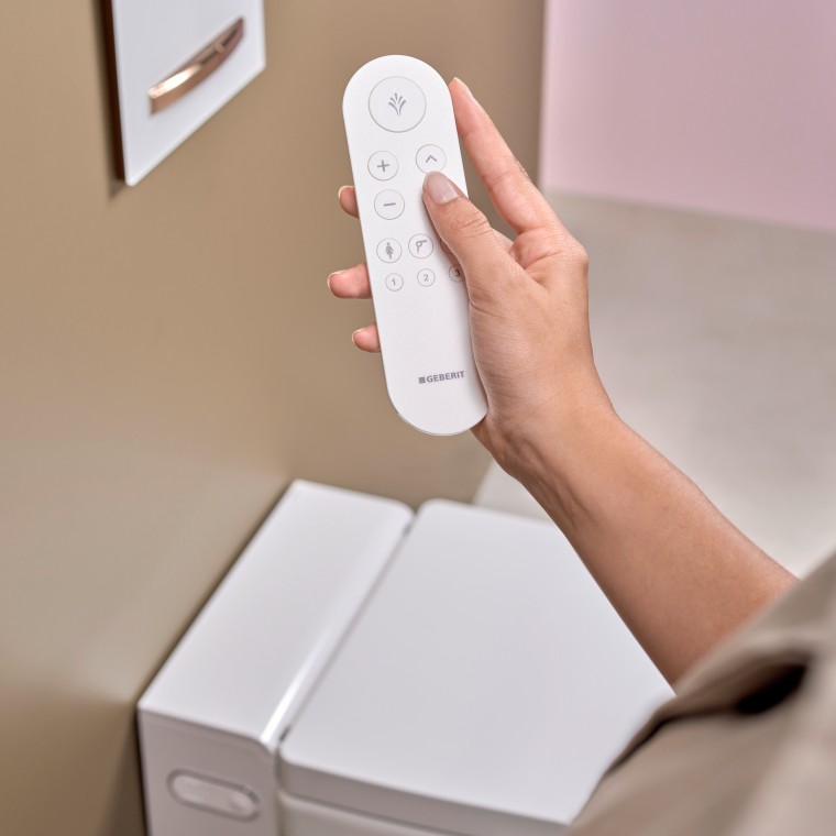 Kobieta trzyma w dłoni pilot do toalety myjącej Geberit Kobieta trzyma w dłoni pilot do toalety myjącej Geberit