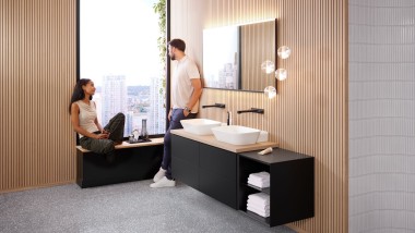 Kobieta siedzi na parapecie w łazience z produktami z serii Geberit ONE i rozmawia z mężczyzną Kobieta siedzi na parapecie w łazience z produktami z serii Geberit ONE i rozmawia z mężczyzną