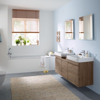 Łazienka rodzinna z jasnoniebieskimi ścianami i meblami łazienkowymi z drewna hikorowego, szafką z lustrem, przyciskiem uruchamiającym i urządzeniami ceramicznymi firmy Geberit
