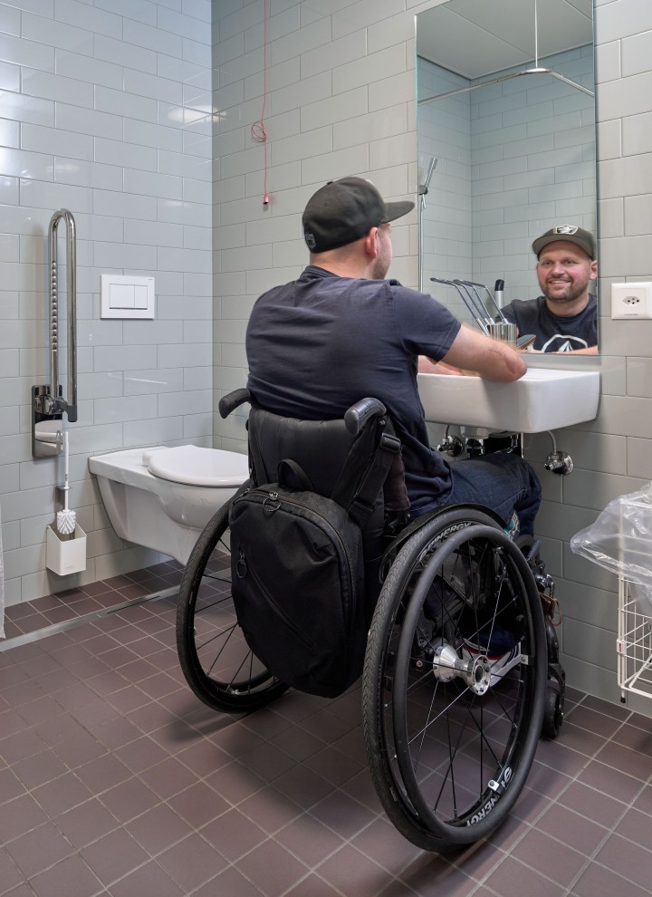 Peter Roos na wózku inwalidzkim przy umywalce w łazience bez barier (© Ben Huggler)