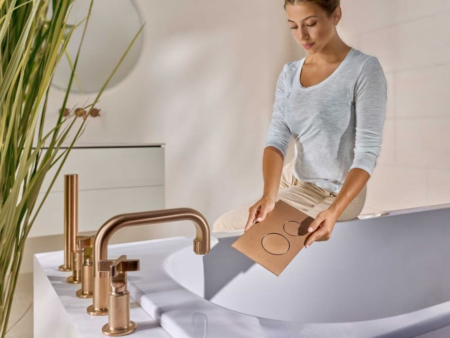 Osoba w łazience z przyciskiem spłukującym Geberit Sigma40 w wykończeniu Brushed Copper, kolorystycznie dopasowanym do armatury Osoba w łazience z przyciskiem spłukującym Geberit Sigma40 w wykończeniu Brushed Copper, kolorystycznie dopasowanym do armatury