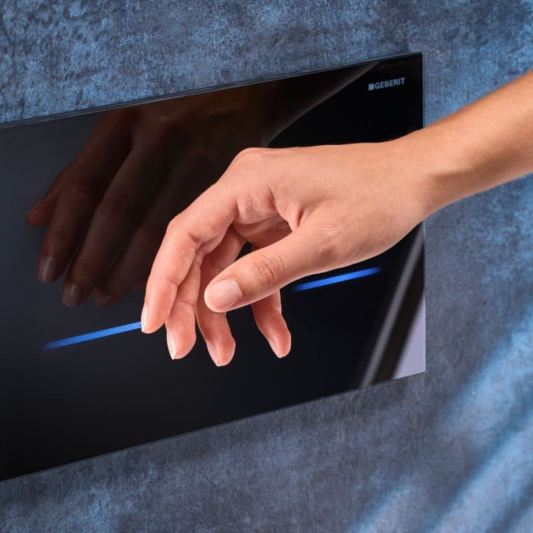 Kobieta zbliża dłoń do czarnego przycisku spłukującego Geberit Kobieta zbliża dłoń do czarnego przycisku spłukującego Geberit