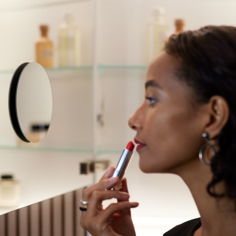 Kobieta maluje usta, patrząc w lustro łazienkowe. Kobieta maluje usta, patrząc w lustro łazienkowe.