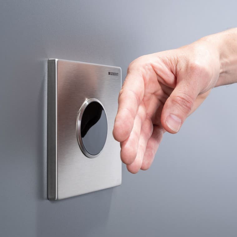 Męska dłoń zbliżona do bezdotykowego przycisku do spłukiwania Geberit Męska dłoń zbliżona do bezdotykowego przycisku do spłukiwania Geberit
